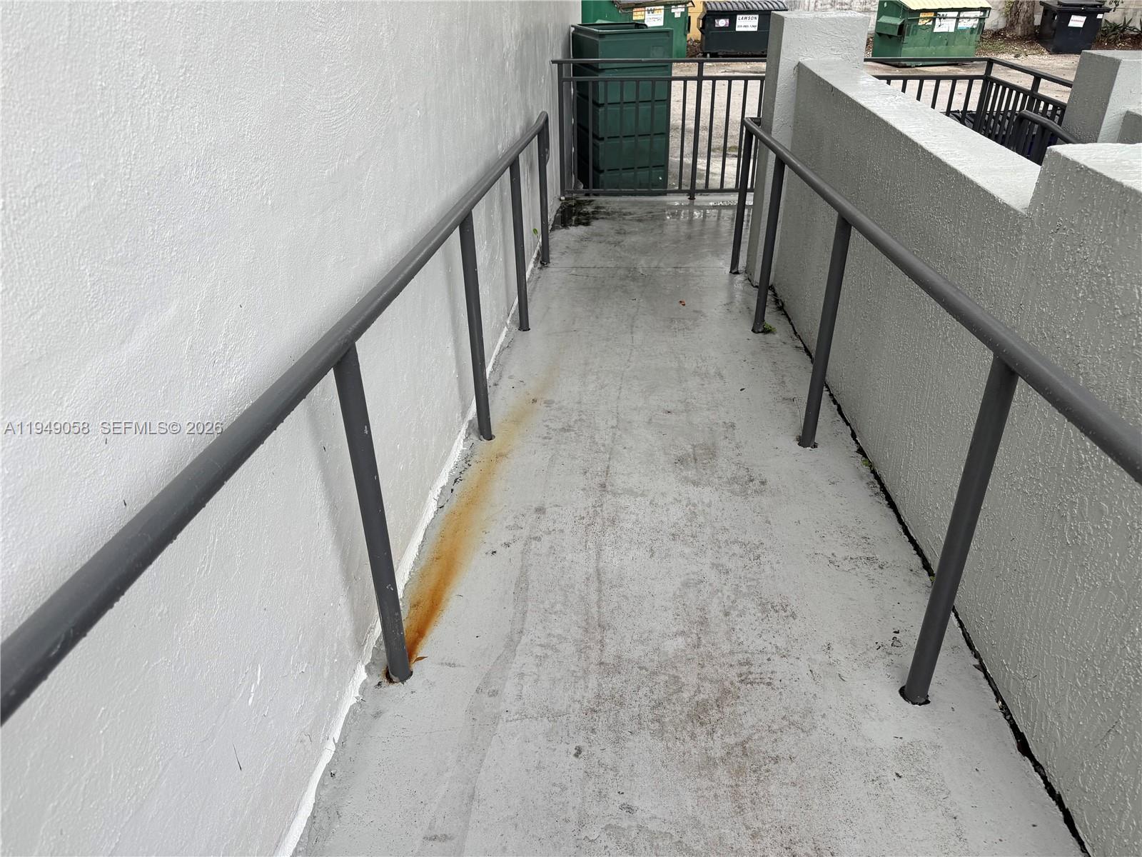 A concrete ramp with metal railings leads toward a gated area with dumpsters — 8347 NW 36th St, Doral FL 33166, DORAL, FL