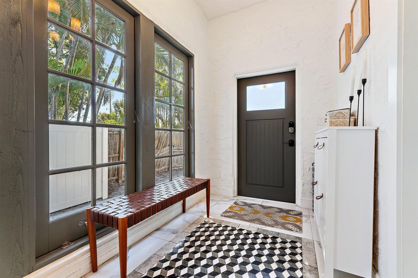 A bright entryway features a dark door, a woven bench, and patterned rugs on tile — 423 Avenida Alegre, West Palm Beach FL 33405, WEST PALM BEACH, FL