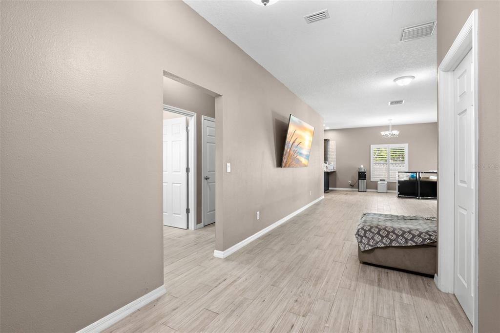 A hallway with light wood-look flooring leads toward an open-concept living area with a television — 7200 62ND WAY N, PINELLAS PARK, FL