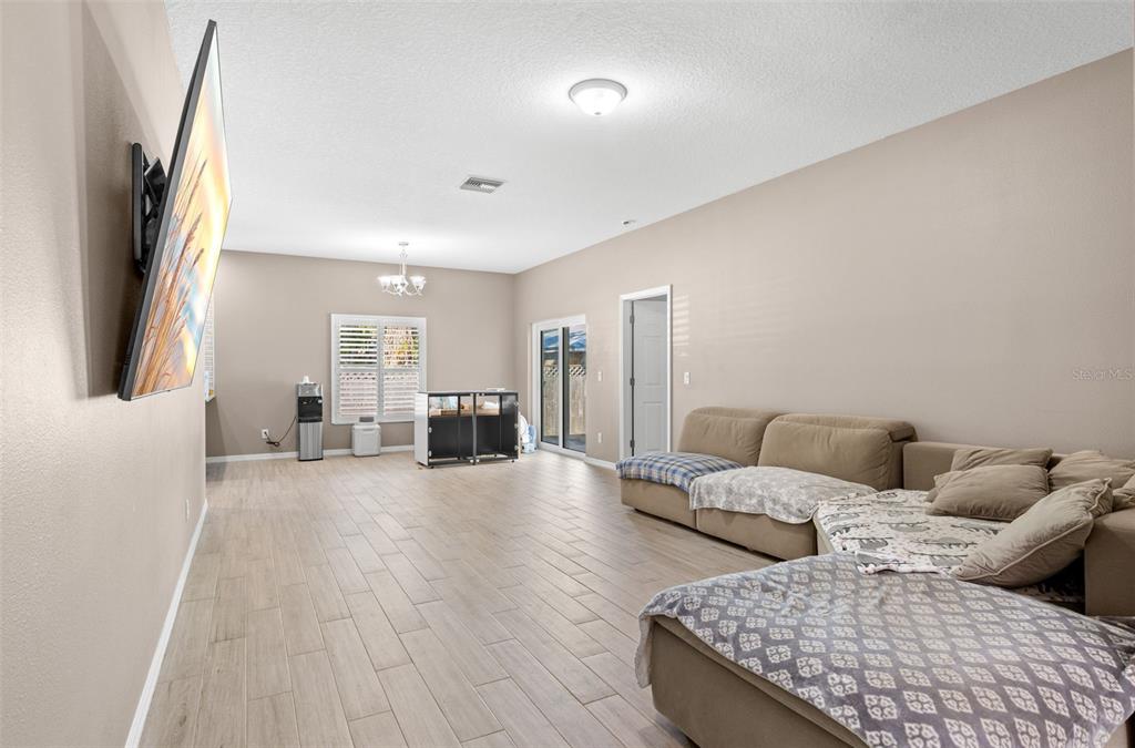 A spacious living room features light tile flooring, beige walls, a large sectional sofa, and television — 7200 62ND WAY N, PINELLAS PARK, FL