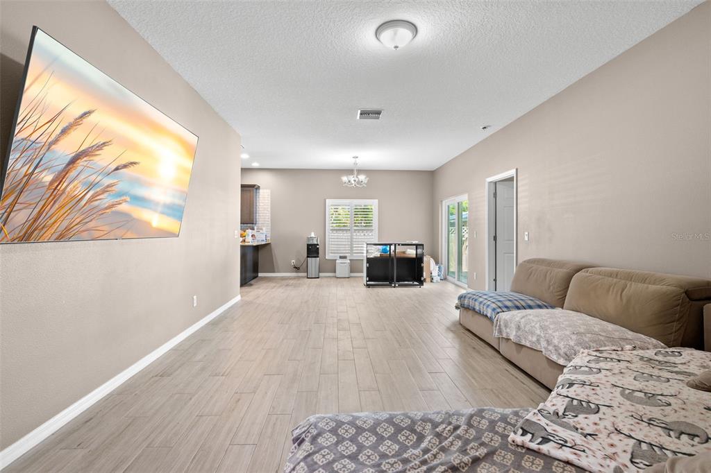 A living room with light wood-look flooring, a large wall-mounted television, and a beige sofa — 7200 62ND WAY N, PINELLAS PARK, FL
