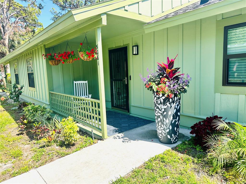 A light green house exterior features a covered porch with hanging plants and a walkway — 5061 BARRINGTON CIRCLE UNIT 1302, SARASOTA, FL