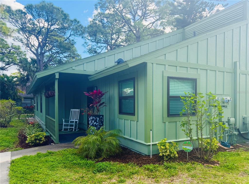 A green house with board and batten siding, a covered porch, and a small front garden — 5061 BARRINGTON CIRCLE UNIT 1302, SARASOTA, FL