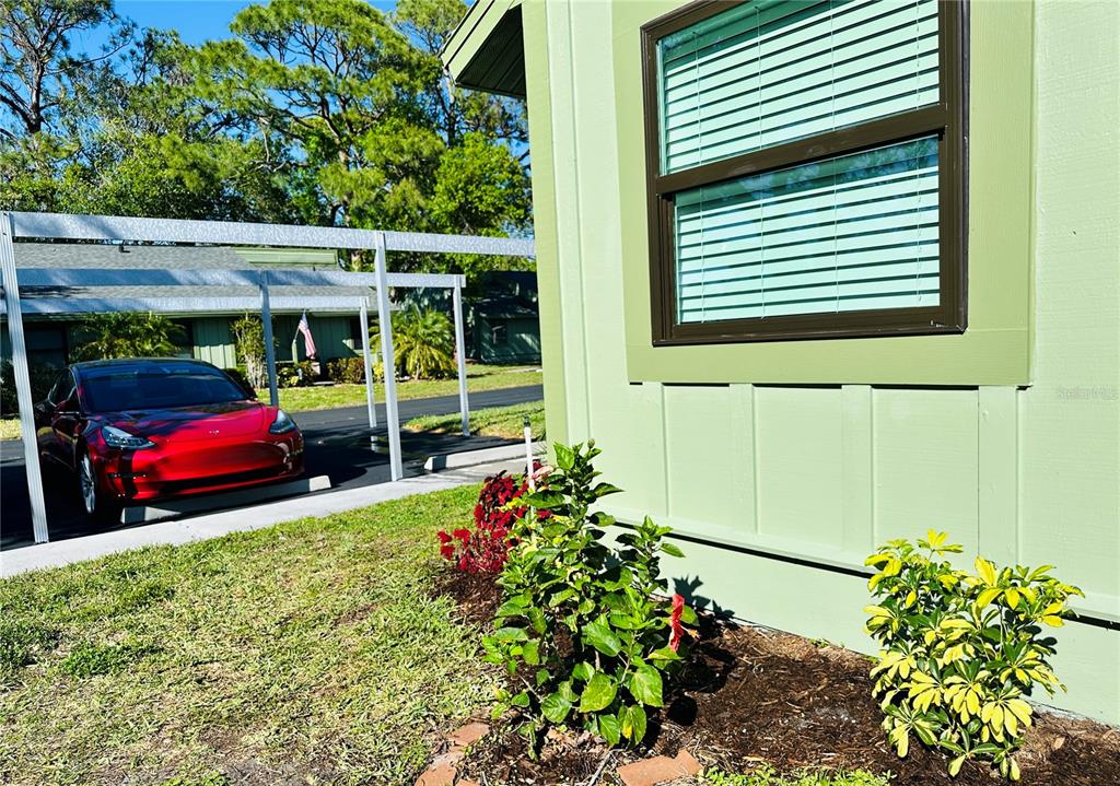 A red car is parked under a carport next to a light green house exterior — 5061 BARRINGTON CIRCLE UNIT 1302, SARASOTA, FL