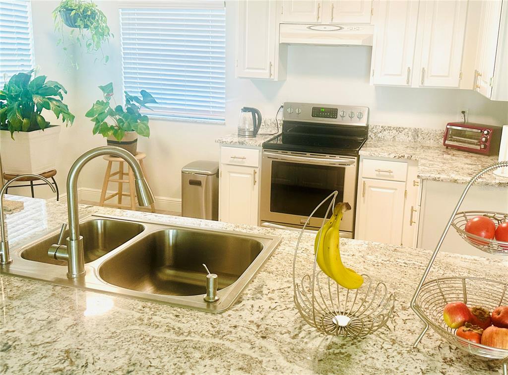 A kitchen features a granite island with a double sink, white cabinets, and stainless appliances — 5061 BARRINGTON CIRCLE UNIT 1302, SARASOTA, FL