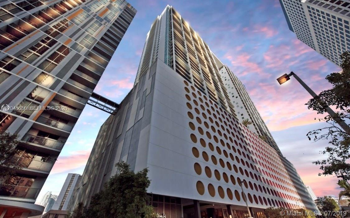 A low-angle exterior view of a modern high-rise building with a distinctive circular-patterned facade — 500 Brickell Ave # 2006, Miami FL 33131, MIAMI, FL
