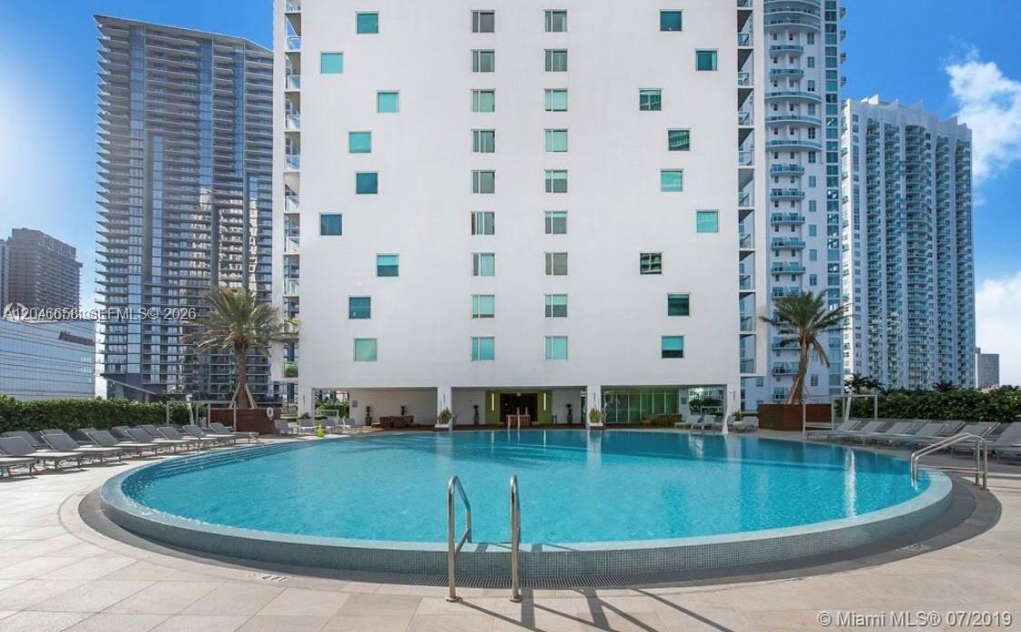 A large outdoor swimming pool sits in front of a tall white residential building — 500 Brickell Ave # 2006, Miami FL 33131, MIAMI, FL
