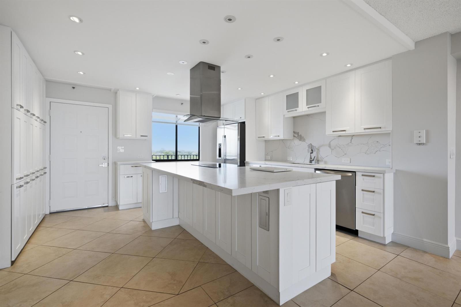 A modern white kitchen features a large marble-topped island, stainless steel appliances, and tile flooring — 2215 Cypress Island Drive # 906, Pompano Beach FL 33069, POMPANO BEACH, FL