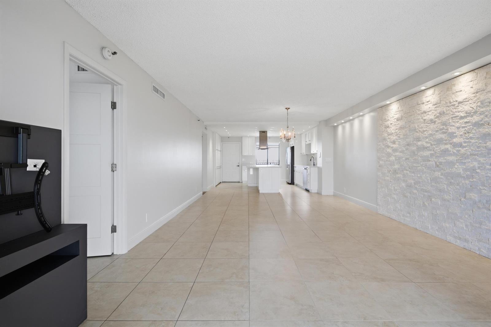 An open-concept living area features large beige floor tiles and a white stone accent wall — 2215 Cypress Island Drive # 906, Pompano Beach FL 33069, POMPANO BEACH, FL