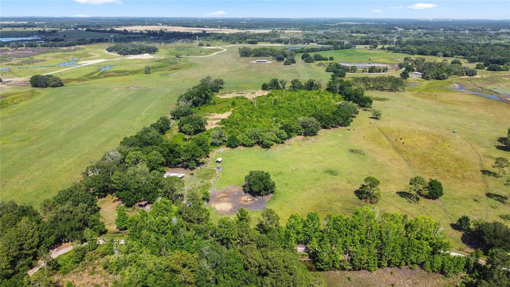 An aerial view shows a large rural property with pastures, wooded areas, and small structures — SE 51ST LANE, CENTER HILL, FL