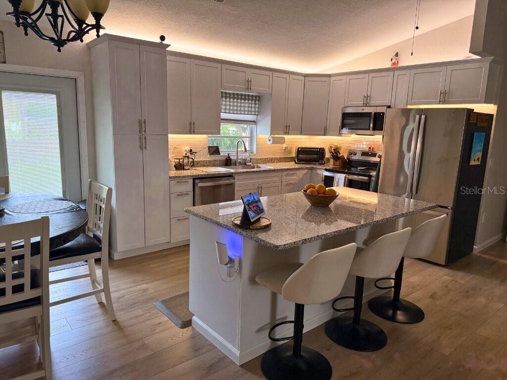 A kitchen features white cabinetry, stainless steel appliances, and a granite-topped island — 7242 ASHMORE DRIVE, NEW PORT RICHEY, FL