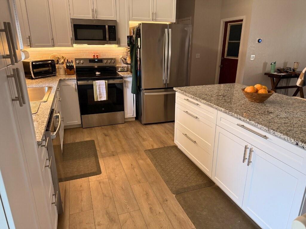 An open-concept kitchen and living area features white cabinetry, a granite island, and wood flooring — 7242 ASHMORE DRIVE, NEW PORT RICHEY, FL