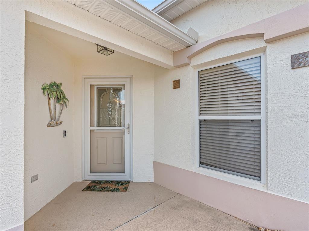 A covered entryway features a white front door with a storm door and a window — 2382 OTHELLO COURT, THE VILLAGES, FL