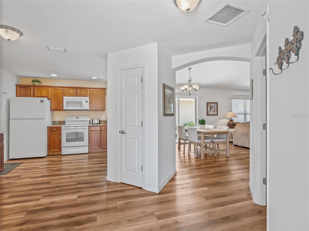 A kitchen with wood cabinets and white appliances opens into a dining area with wood flooring — 2382 OTHELLO COURT, THE VILLAGES, FL