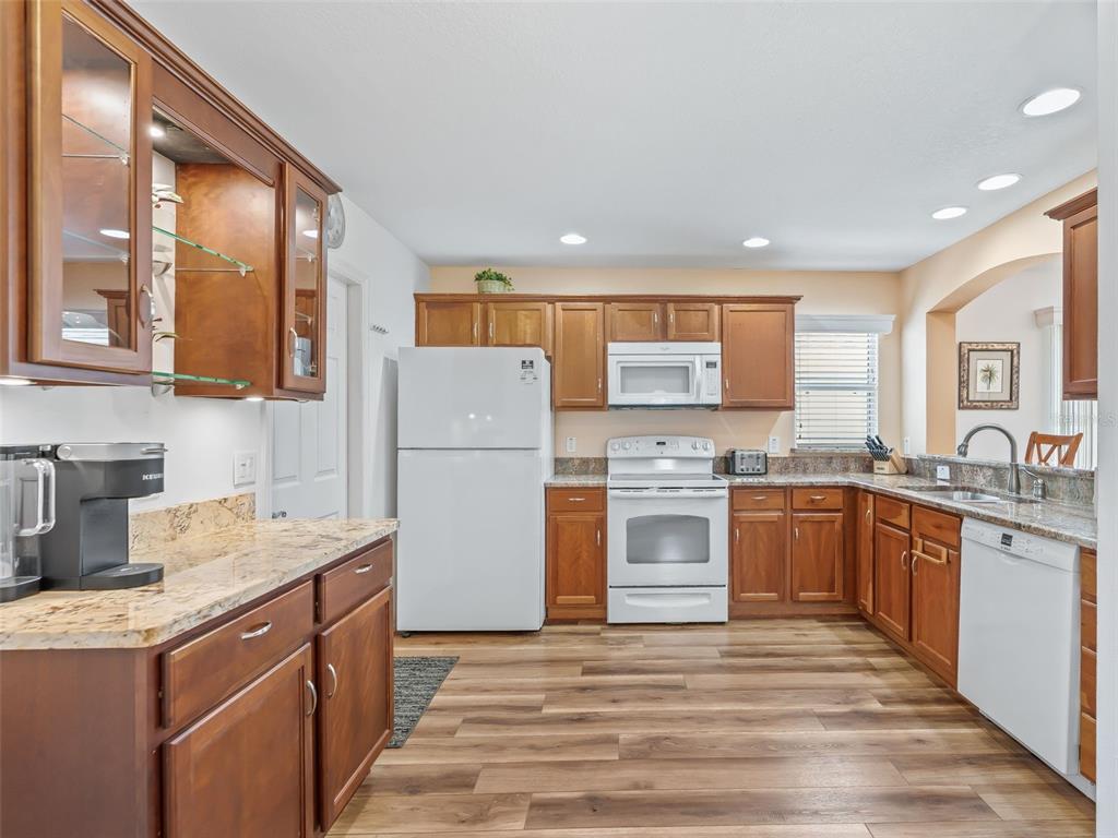 A kitchen features wood cabinets, granite countertops, white appliances, and wood-look flooring — 2382 OTHELLO COURT, THE VILLAGES, FL