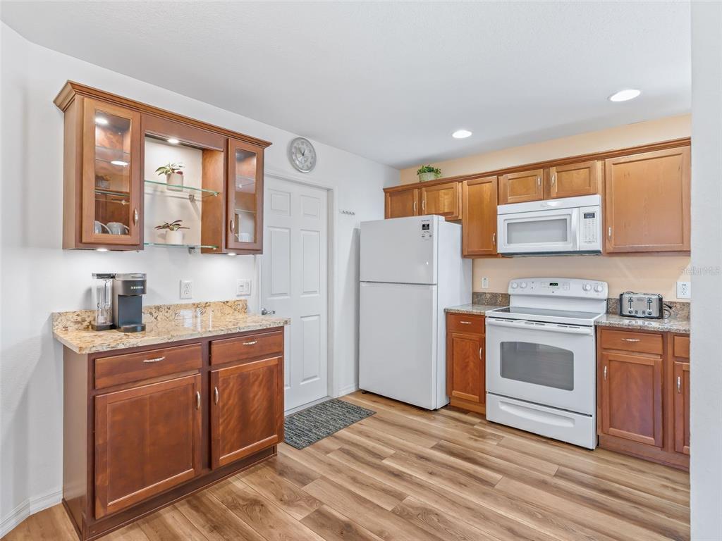 A kitchen with wood cabinets, granite countertops, white appliances, and wood-look flooring — 2382 OTHELLO COURT, THE VILLAGES, FL