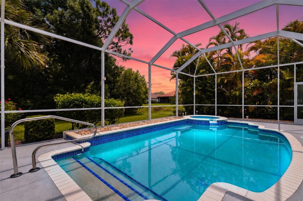 A screened-in swimming pool and spa with blue tile trim under a vibrant sunset sky — 4364 CORSO VENETIA BOULEVARD, VENICE, FL