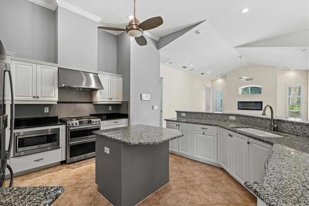 A kitchen with white cabinets, granite countertops, a gray island, and stainless steel appliances — 4364 CORSO VENETIA BOULEVARD, VENICE, FL