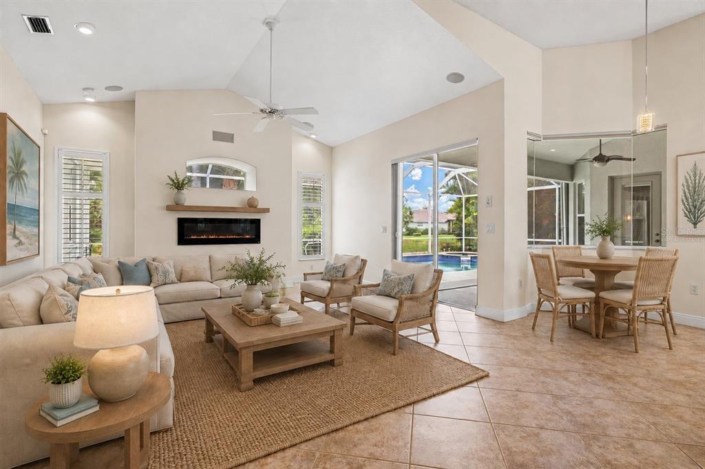 A living room with a fireplace, vaulted ceiling, and sliding glass doors opening to a pool — 4364 CORSO VENETIA BOULEVARD, VENICE, FL