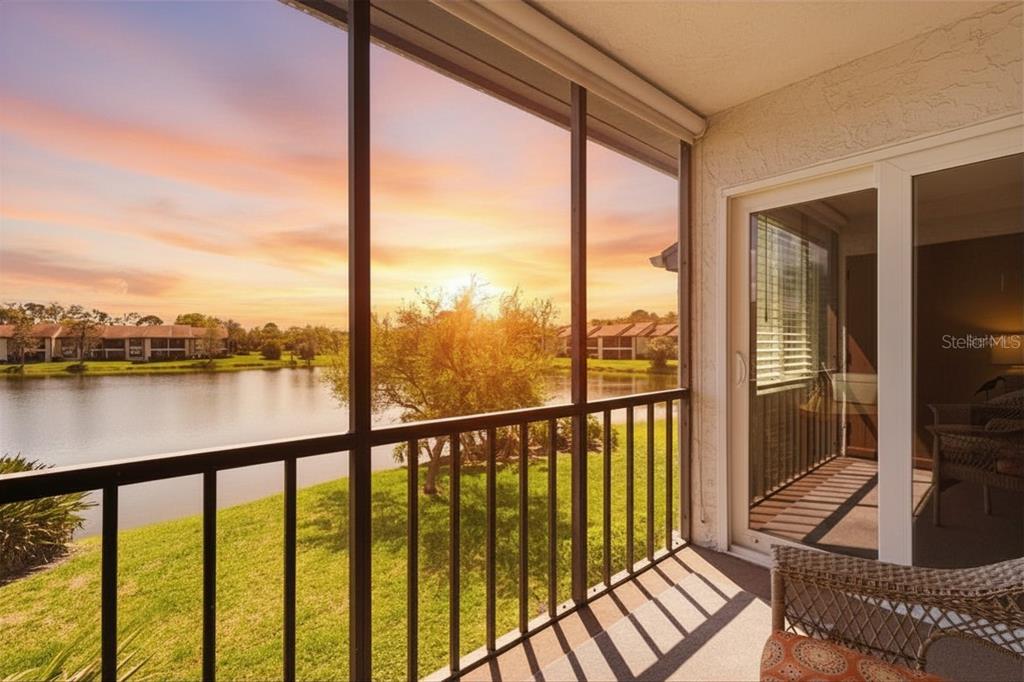 A screened-in balcony overlooks a lake at sunset with a sliding glass door entrance — 240 CYPRESS LANE UNIT 240, OLDSMAR, FL