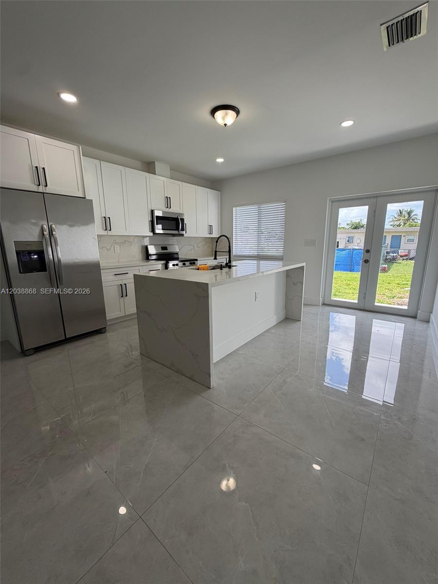 A modern kitchen features white cabinets, stainless steel appliances, a marble-topped island, and tile flooring — 12080 & 12090 SW 213th St, Miami FL 33177, MIAMI, FL