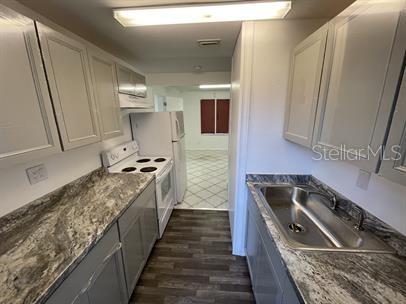 A galley kitchen features gray cabinets, granite-look countertops, a white stove, and a stainless sink — 15 S DOLLINS AVENUE, ORLANDO, FL