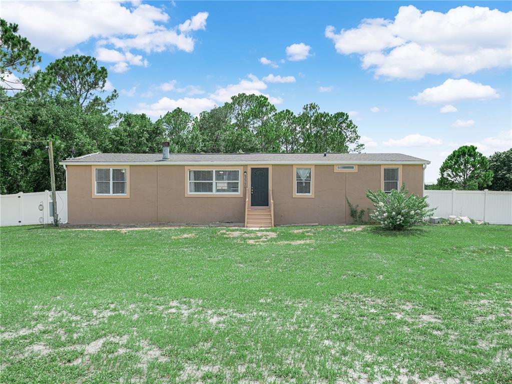 A single-story house with tan stucco siding, a dark front door, and a grassy yard — 3559 REAGAN BOULEVARD, LAKE WALES, FL