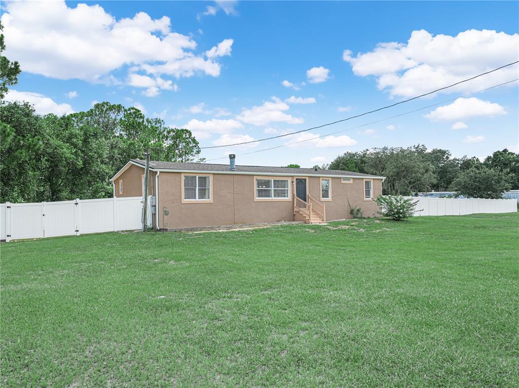 A single-story tan house with a white vinyl fence sits on a large grass lawn — 3559 REAGAN BOULEVARD, LAKE WALES, FL