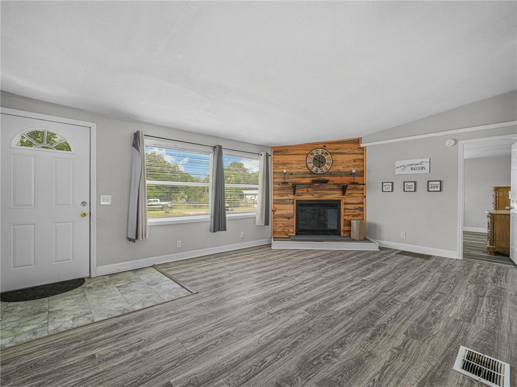 A living room features wood-look flooring, a corner fireplace with wood paneling, and a front door — 3559 REAGAN BOULEVARD, LAKE WALES, FL