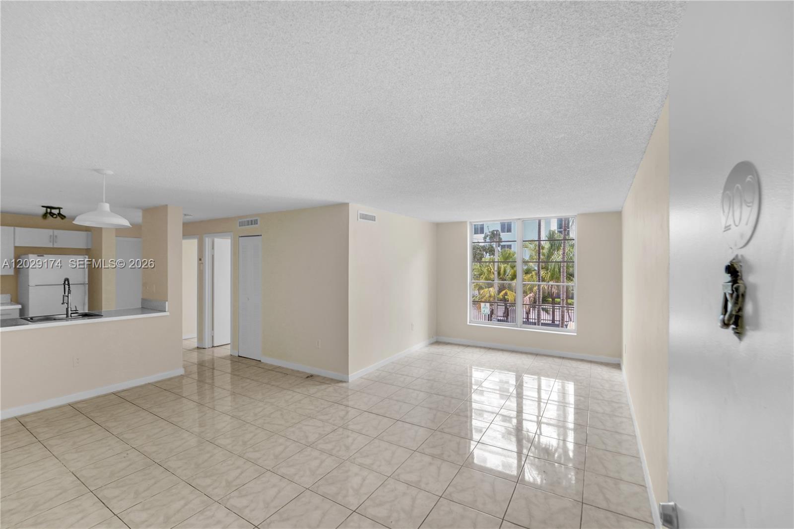 An open-concept living area features beige tile flooring, a kitchen pass-through, and a large window — 210 SW 11th St # 209, Miami FL 33130, MIAMI, FL