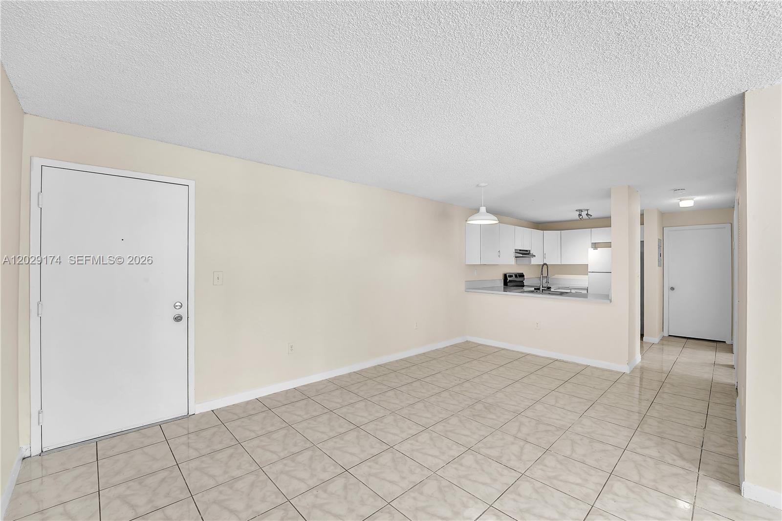 An open-concept living area features beige tile flooring, a white front door, and a kitchen — 210 SW 11th St # 209, Miami FL 33130, MIAMI, FL