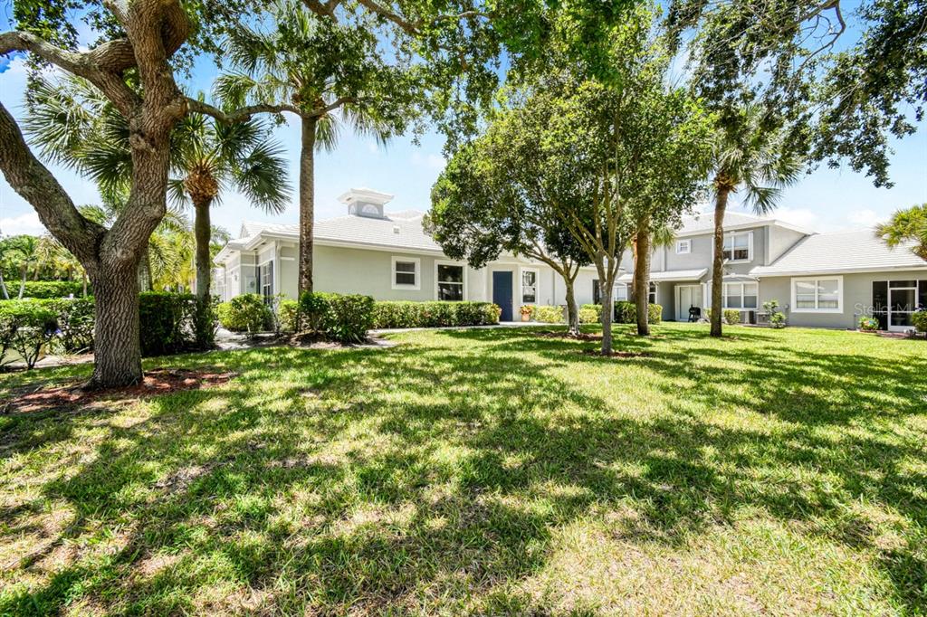 A grassy lawn leads to the exterior of a light-colored house with mature trees — 4952 SOUTHARD STREET, GREENACRES, FL