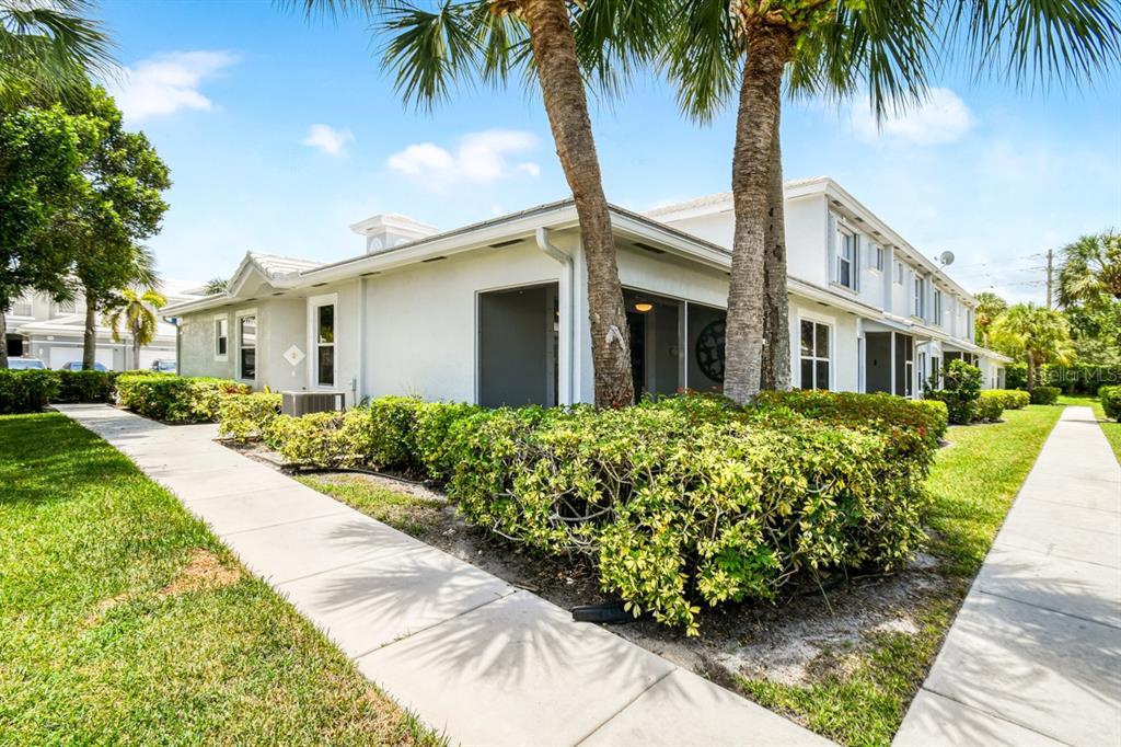 A sidewalk leads past a landscaped hedge toward the screened patio of a white townhouse — 4952 SOUTHARD STREET, GREENACRES, FL