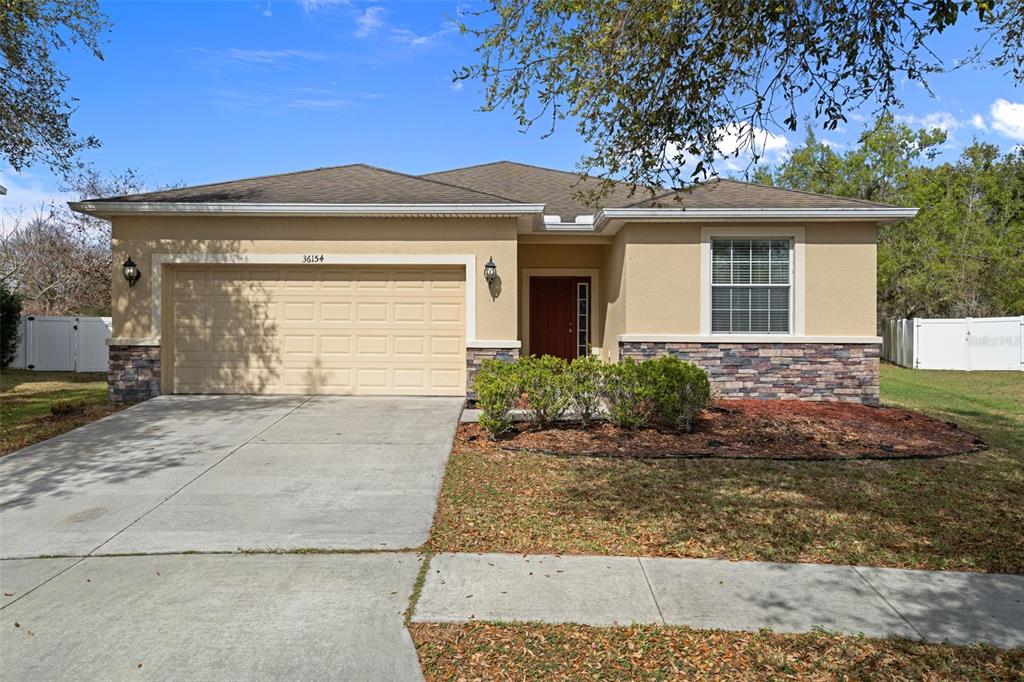 A single-story house with a beige stucco exterior, stone accents, and a two-car garage — 36154 LAGUNA HILLS CIRCLE, ZEPHYRHILLS, FL