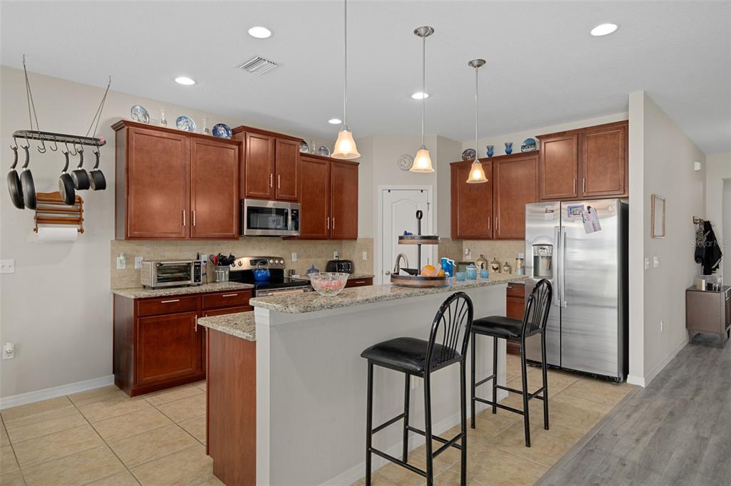 A kitchen features wood cabinets, granite countertops, a breakfast bar with stools, and stainless appliances — 36154 LAGUNA HILLS CIRCLE, ZEPHYRHILLS, FL