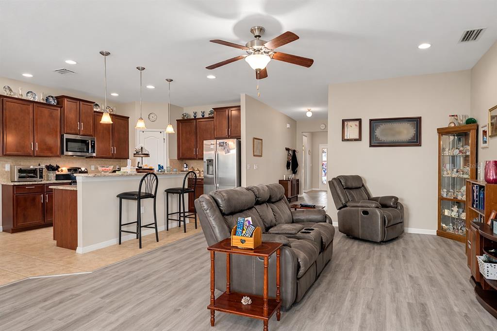 An open-concept living room and kitchen featuring wood cabinetry, stainless steel appliances, and gray flooring — 36154 LAGUNA HILLS CIRCLE, ZEPHYRHILLS, FL