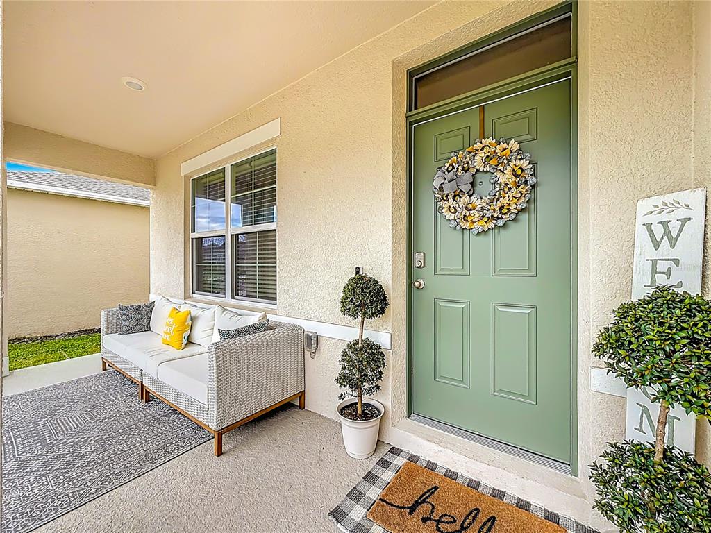 A covered front porch features a green door, a white sofa, and potted topiary trees — 3723 PARAGON LANE, CLERMONT, FL