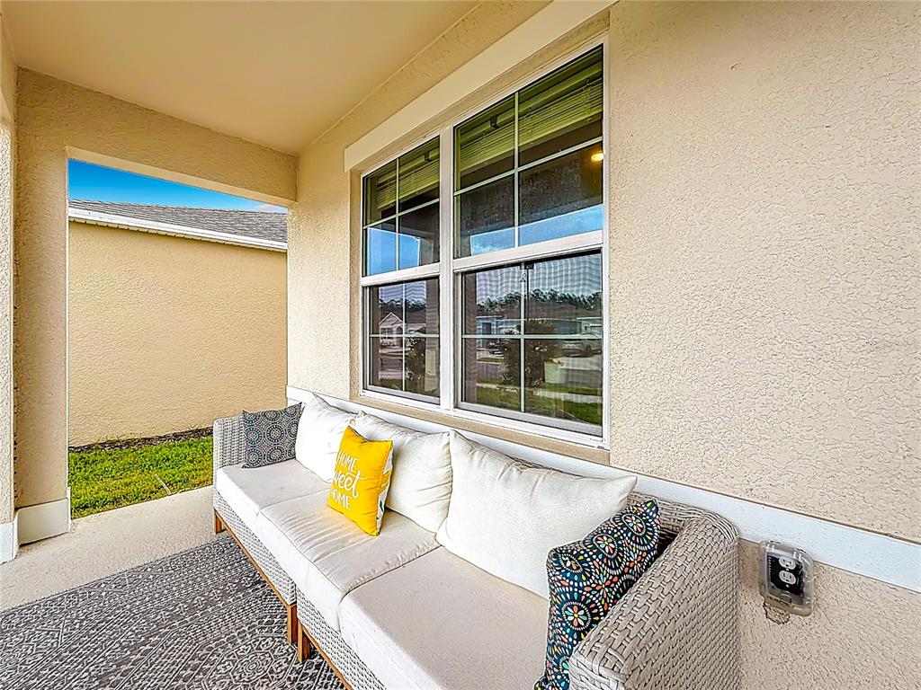 A covered patio features a wicker sofa with decorative pillows placed against a beige wall — 3723 PARAGON LANE, CLERMONT, FL