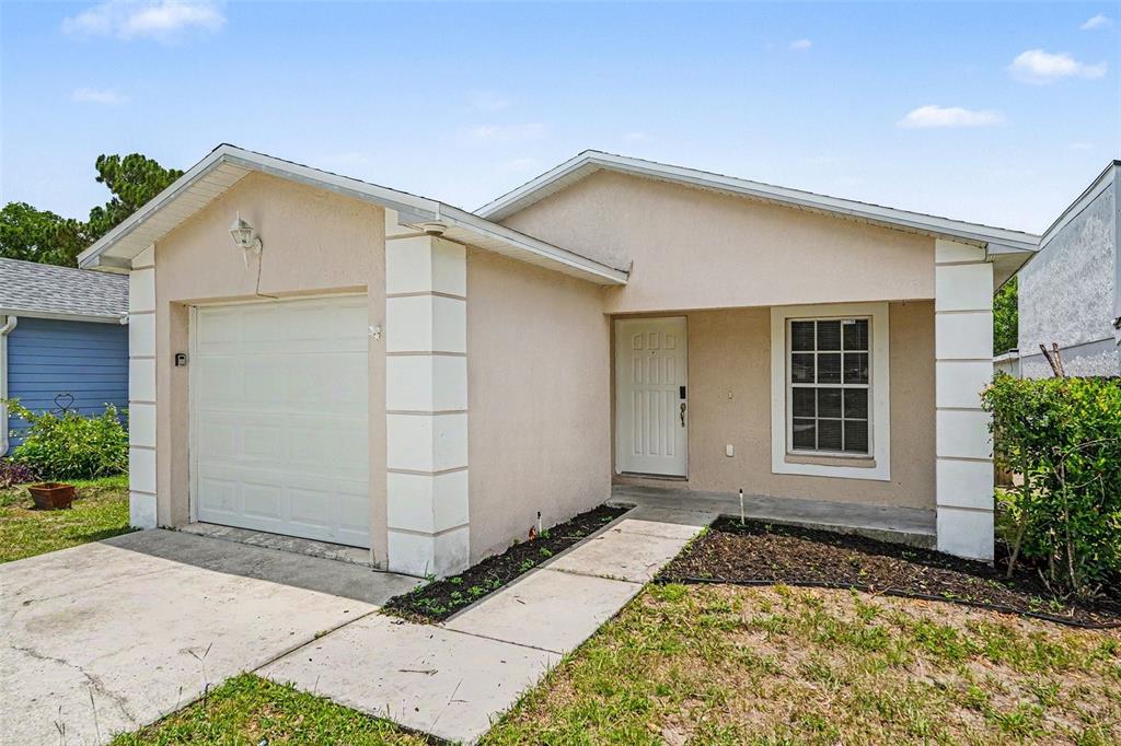 A single-story house with beige stucco siding, a white garage door, and a front porch — 23110 DOVER DRIVE, LAND O LAKES, FL