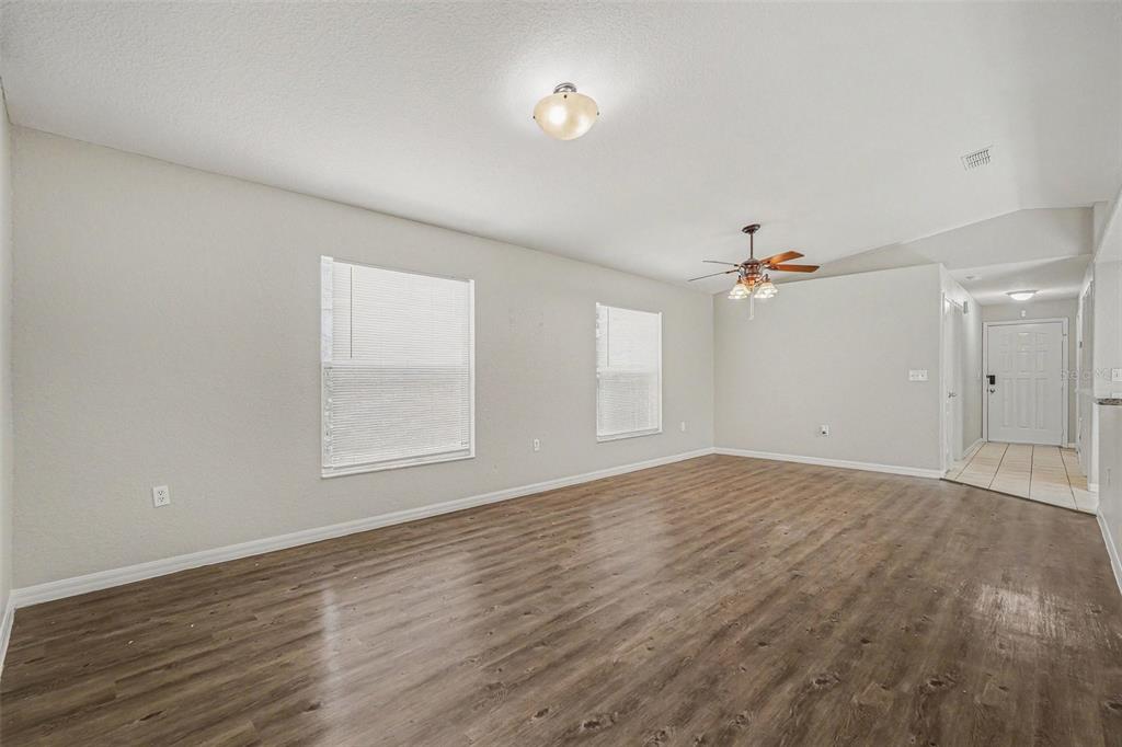 An empty living room features wood-look flooring, light-colored walls, two windows, and a ceiling fan — 23110 DOVER DRIVE, LAND O LAKES, FL