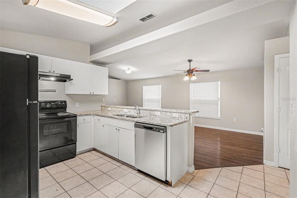 A kitchen with white cabinets, granite countertops, and black appliances opens to a living area — 23110 DOVER DRIVE, LAND O LAKES, FL