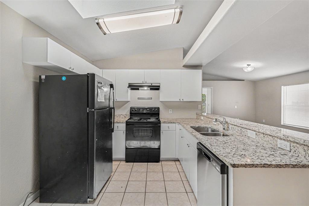A kitchen features white cabinets, granite countertops, black appliances, and light-colored tile flooring — 23110 DOVER DRIVE, LAND O LAKES, FL