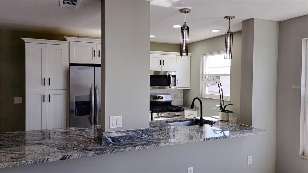 A kitchen features white cabinets, stainless steel appliances, and a granite countertop breakfast bar — 5623 80TH ST N UNIT 510, ST PETERSBURG, FL