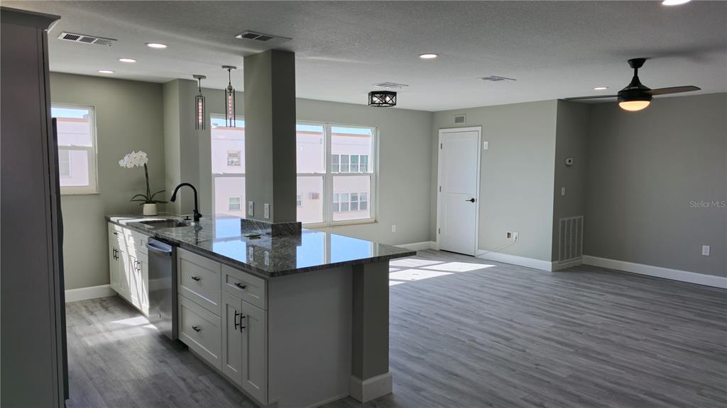 A kitchen with a granite island, white cabinets, and gray flooring opens into a living area — 5623 80TH ST N UNIT 510, ST PETERSBURG, FL