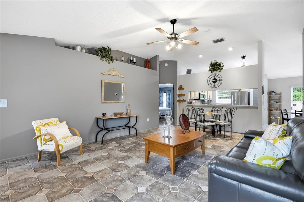A living room with tiled floors, a dark leather sofa, and an adjacent dining area — 11026 STREAMSIDE DRIVE, TAMPA, FL