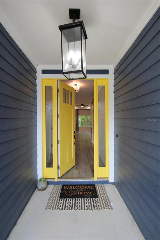 A bright yellow front door with side windows opens into a home with wood flooring — 4102 NW 26TH DRIVE, GAINESVILLE, FL