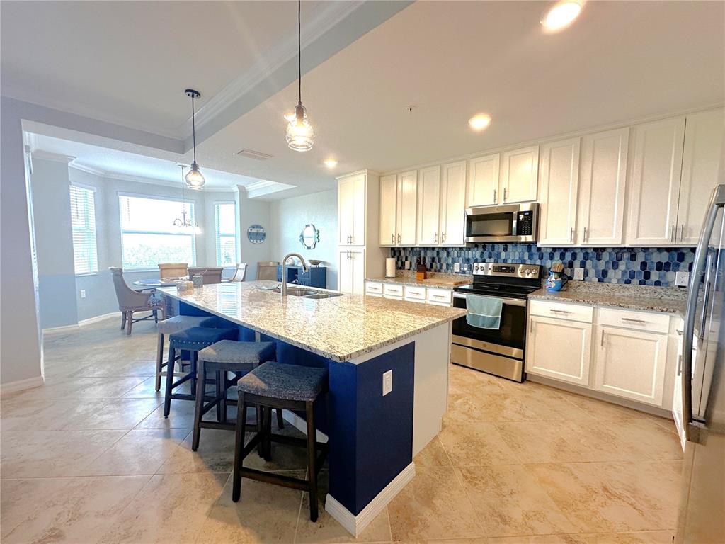 A kitchen features white cabinets, a granite-topped island with blue base, and tile flooring — 14081 HERITAGE LANDING BOULEVARD UNIT 223, PUNTA GORDA, FL