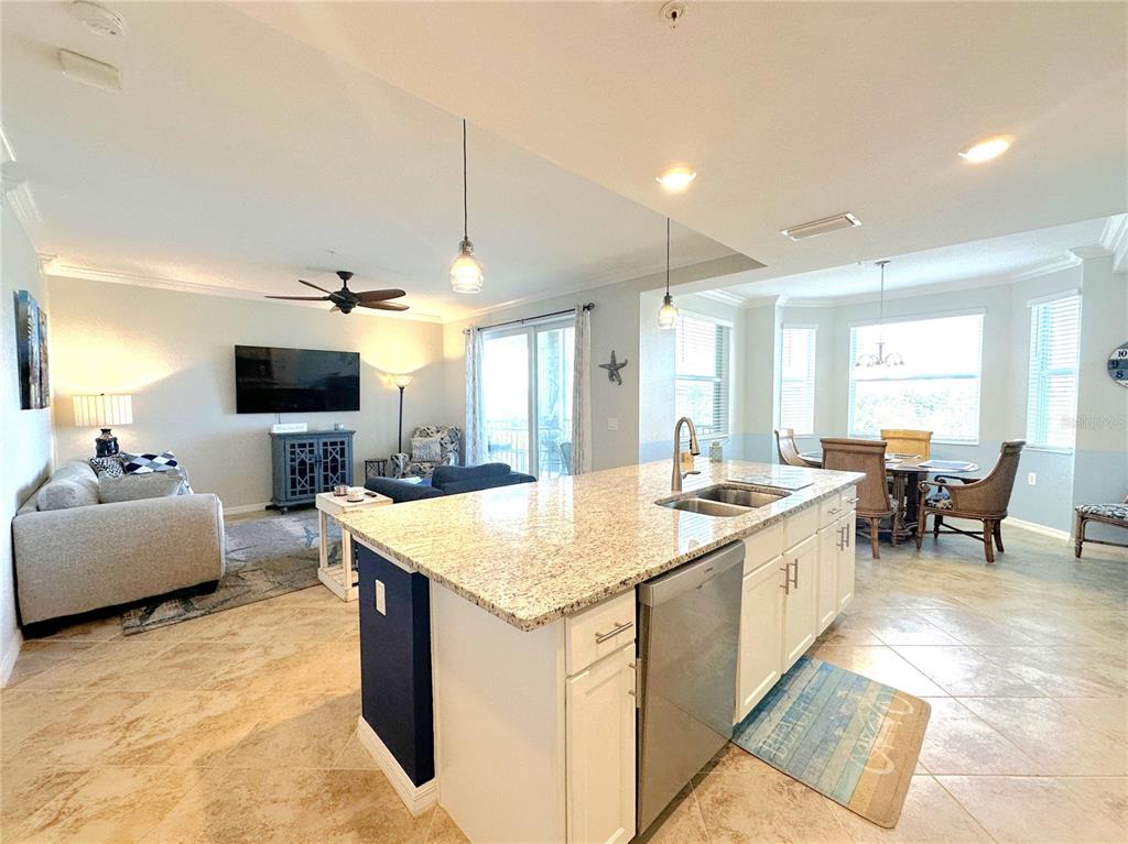 An open-concept kitchen with granite countertops and stainless steel appliances overlooks a living room — 14081 HERITAGE LANDING BOULEVARD UNIT 223, PUNTA GORDA, FL