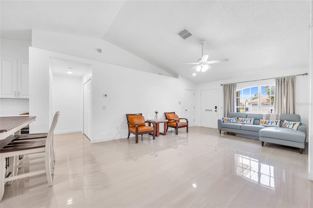 A bright living room features white walls, tile flooring, a vaulted ceiling, and a sofa — 4211 FLOATING ORCHID COURT, ST CLOUD, FL