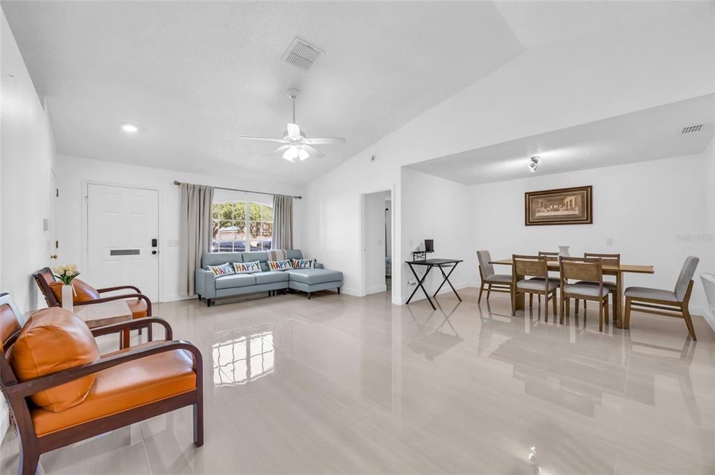 A bright, open-concept living and dining area features white walls, tile flooring, and vaulted ceilings — 4211 FLOATING ORCHID COURT, ST CLOUD, FL